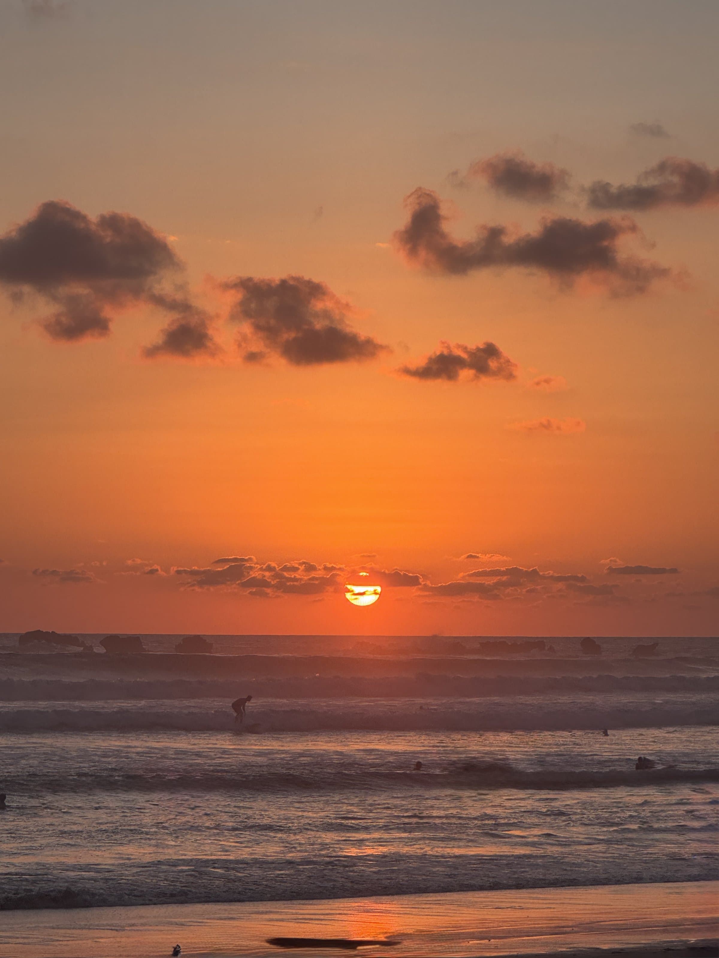 Sunset at Playa Guiones, the sun on the horizon and surfers in the water
